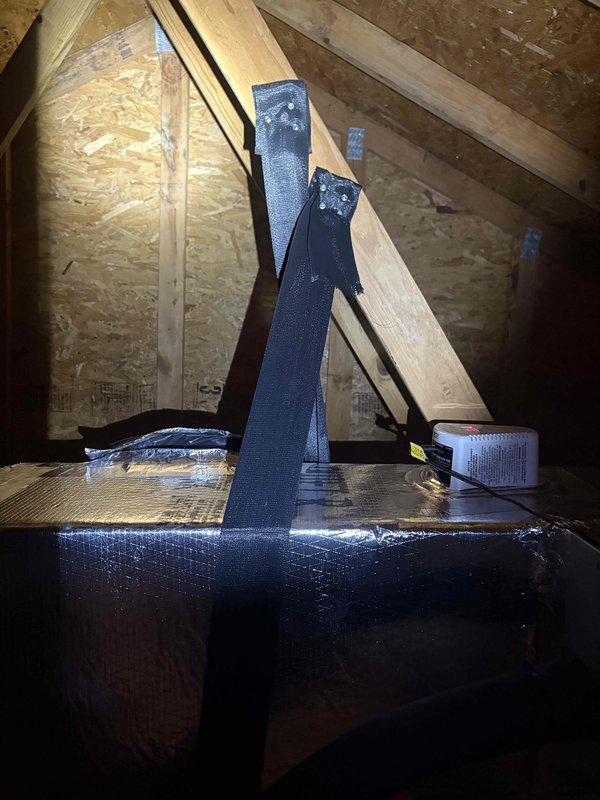 Completed management-requested return visit to attic for visual documentation of condensate line trap and installed additional hanger support on return ductwork to prevent future collapse. Photographed existing condensate trap configuration and secured reflective-wrapped rectangular return duct with black strapping to maintain proper positioning and structural integrity.