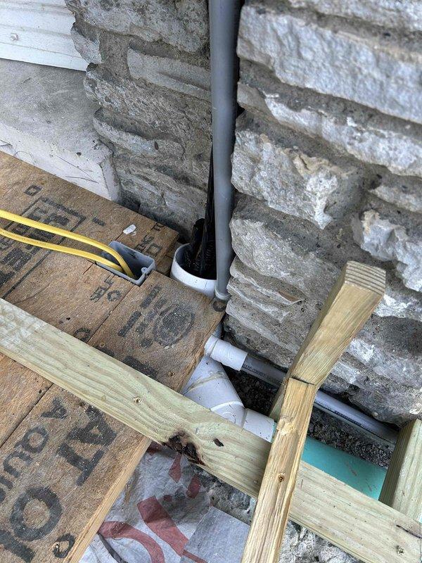 Installed condensate drain line routing through floor opening to accommodate upcoming concrete pour. PVC piping was stubbed up into sunroom area and extended to exterior, with rough framing opening maintained for future access and proper drainage system connection once foundation work is completed.