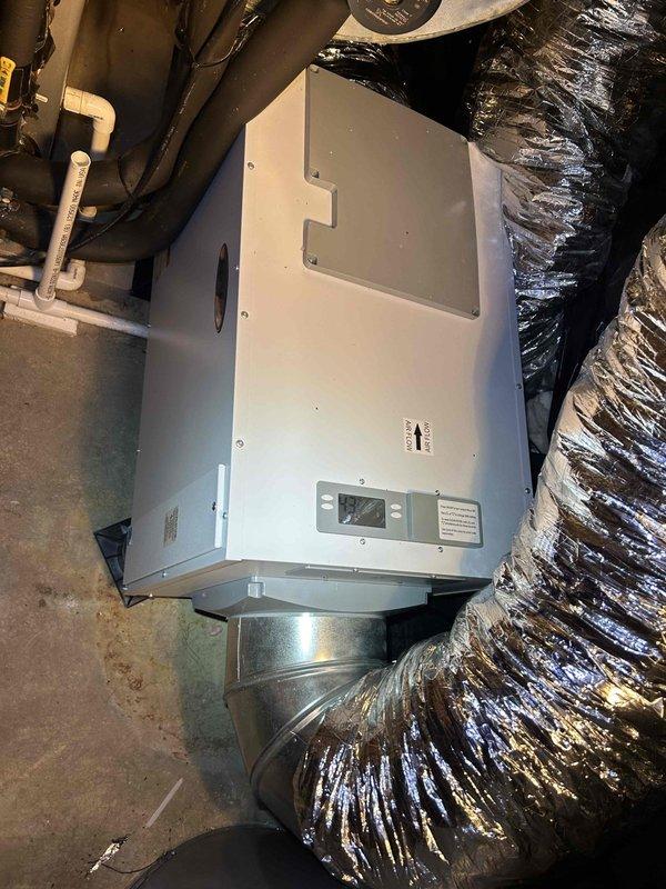 Completed comprehensive HVAC maintenance on a 16-year-old air conditioning system, including installation of a compressor saver kit to extend equipment life and improve efficiency. Performed AC tune-up procedures, cleaned steam humidifier components, and serviced dehumidifier unit using customer-provided canister and dynamic filters. Documented existing equipment condition showing dust accumulation on air handler components and ductwork, with photos capturing the attic-mounted unit, metallic transition plenum, flexible aluminum ductwork, and PVC condensate drainage system.