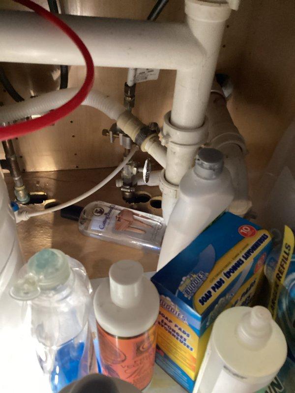Completed routine plumbing inspection of residential property, examining under-sink cabinet plumbing system and utility room piping infrastructure. Inspected kitchen sink drain assembly including PVC piping, P-trap configuration, supply line connections, and shut-off valves; utility room inspection revealed multiple vertical and horizontal PVC pipe runs with brass valve assemblies in functional condition, though area showed signs of age and accumulated debris.