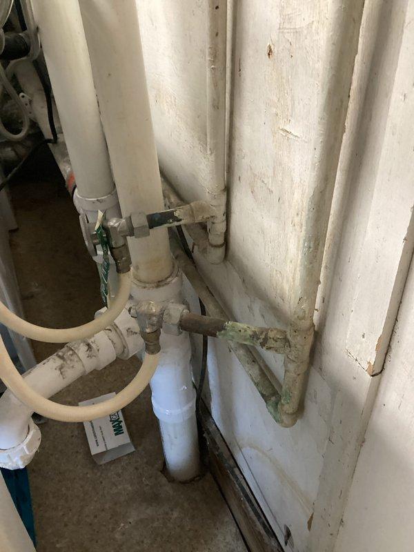 Completed routine plumbing inspection of residential property, examining under-sink cabinet plumbing system and utility room piping infrastructure. Inspected kitchen sink drain assembly including PVC piping, P-trap configuration, supply line connections, and shut-off valves; utility room inspection revealed multiple vertical and horizontal PVC pipe runs with brass valve assemblies in functional condition, though area showed signs of age and accumulated debris.