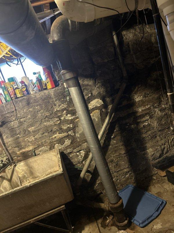 Responded to service call for leak in major bathroom pipe requiring inspection and estimate. Upon arrival, accessed unfinished basement area with exposed stone foundation to locate source of water intrusion. Conducted thorough inspection of vertical drainage system including large gray PVC piping running along foundation wall and cream-colored PVC pipe with metal clamps in crawl space area. Assessed condition of plumbing infrastructure, connections, and surrounding mechanical systems. Documented findings with photographs showing pipe configuration, mounting hardware, and basement environment for accurate estimate preparation. Provided customer with detailed assessment of leak location and recommended repair options for the affected drainage line.