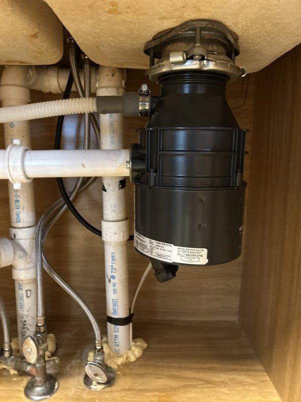 Responded to service call for non-operational garbage disposal unit. Upon arrival, assessed Whirlpool Model GC2000PE3 (1/2 HP, 120V, 60Hz, 6.9A) that was previously producing humming noise but currently had no power. Unit had been previously repaired and was of unknown age. Performed diagnostic inspection of disposal unit, electrical connections, and under-sink plumbing configuration. Documented existing installation including mounting assembly, drain connections, P-trap configuration, and electrical wiring. Photographed kitchen sink setup with double-basin configuration and complete under-cabinet plumbing system for service records.