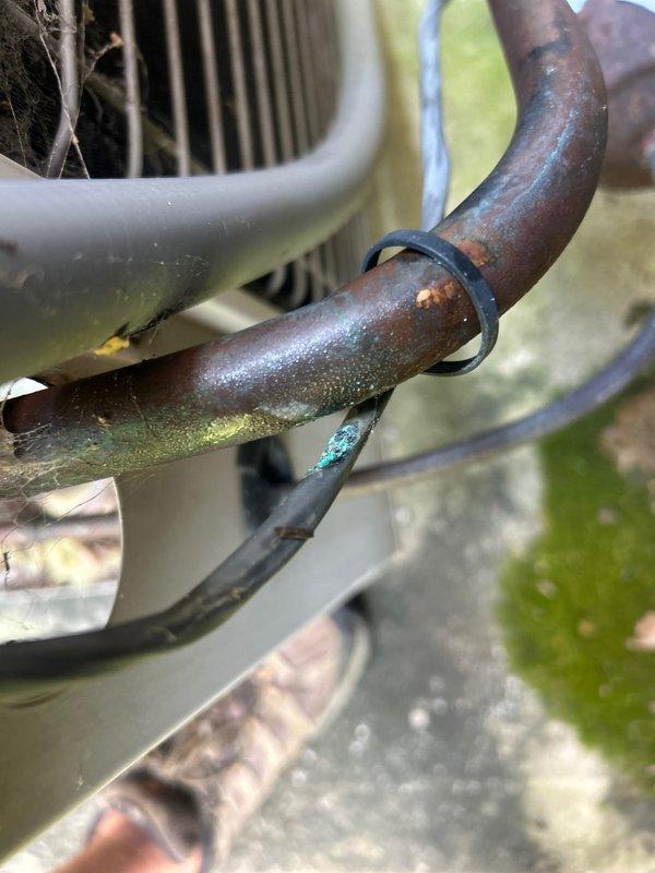 Responded to no cooling complaint on 10+ year old electric upstairs AC unit with reported no airflow. Upon arrival, performed system diagnostics and inspection of both indoor and outdoor equipment. Discovered outdoor condenser unit experiencing significant operational issues. Inspection revealed extensive corrosion and oxidation on refrigerant line set, including copper suction line showing advanced deterioration with rust-colored and greenish patina buildup. Condenser fan motor housing showed signs of age and weathering. Corroded refrigerant lines compromised system integrity and likely contributing to loss of cooling capacity and airflow issues. Documented equipment condition with photographic evidence showing deteriorated copper piping, corroded components, and aging outdoor unit assembly. Given the age of the system and extent of component deterioration, provided assessment and repair options to restore cooling function.