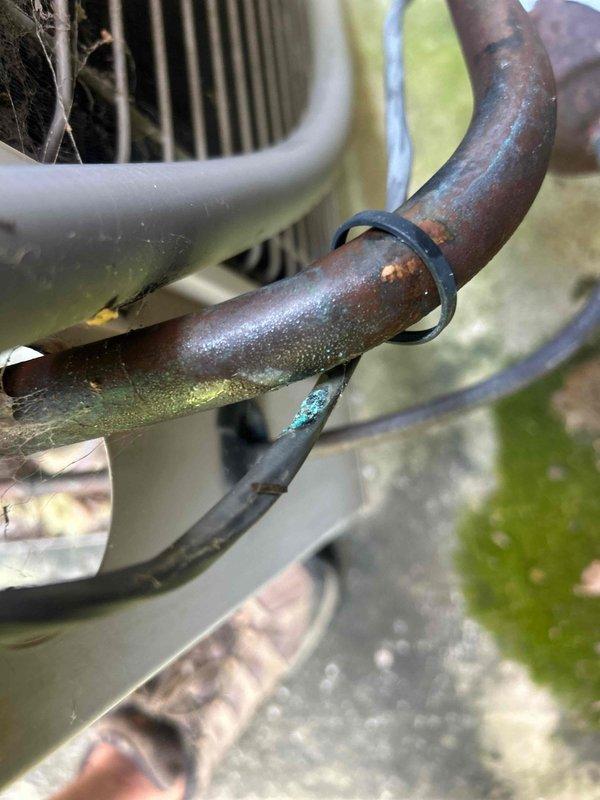 Responded to no cooling complaint on 10+ year old electric upstairs AC unit with reported no airflow. Upon arrival, performed system diagnostics and inspection of both indoor and outdoor equipment. Discovered outdoor condenser unit experiencing significant operational issues. Inspection revealed extensive corrosion and oxidation on refrigerant line set, including copper suction line showing advanced deterioration with rust-colored and greenish patina buildup. Condenser fan motor housing showed signs of age and weathering. Corroded refrigerant lines compromised system integrity and likely contributing to loss of cooling capacity and airflow issues. Documented equipment condition with photographic evidence showing deteriorated copper piping, corroded components, and aging outdoor unit assembly. Given the age of the system and extent of component deterioration, provided assessment and repair options to restore cooling function.