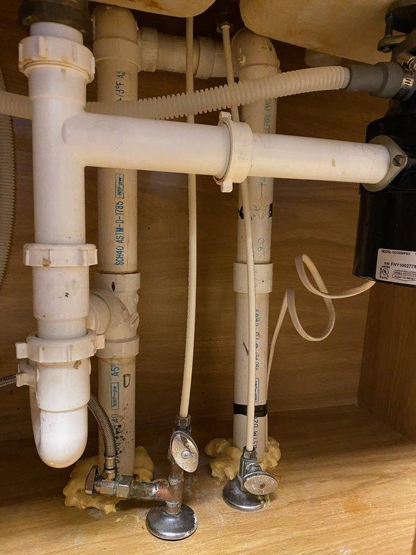 Responded to callback for improperly installed Whirlpool garbage disposal Model GC2000PE3 that was hardwired instead of utilizing the factory plug configuration, creating a potential fire hazard. Documented existing installation with photographs showing under-sink plumbing configuration, PVC drain assembly, supply lines, and disposal electrical connections for management review and assessment of corrective action needed.