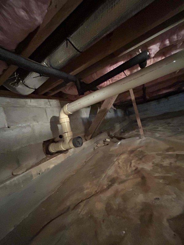 Responded to service call for drainage issue occurring during washing machine spin cycle, potentially related to previous clog. Accessed crawl space to inspect plumbing system and identify source of backup. Located and examined drainage lines serving laundry area, including PVC piping and connections between floor joists. Inspected pipe routing, fittings, and joints for blockages, improper slope, or structural issues affecting drainage flow. Assessed condition of existing plumbing infrastructure in confined space beneath structure. Documented findings with photos showing pipe configuration, insulation clearances, and overall system layout for customer records and future reference.