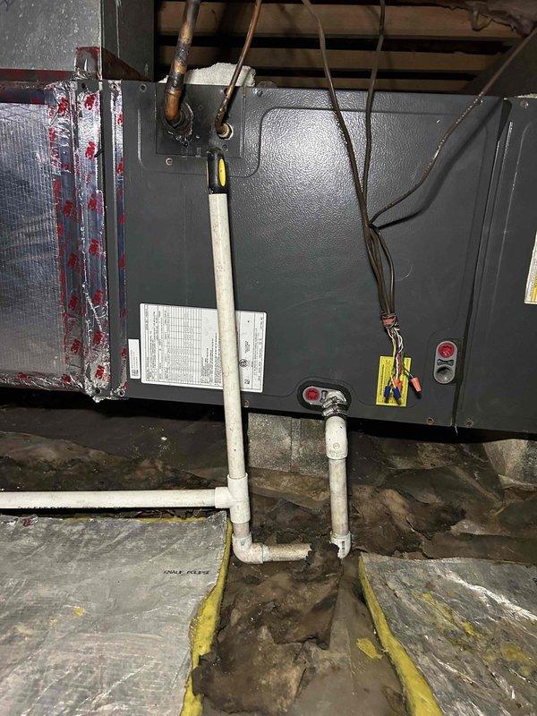 Conducted site assessment of HVAC air handler installation in attic space and crawlspace area to provide estimate for rerouting condensate drainage line. Evaluated existing white PVC condensate piping configuration running through crawlspace with multiple elbows and joints, noting moisture exposure concerns and deteriorated foundation conditions. Documented current air handler setup with connected refrigerant lines, electrical connections, and condensate drain routing to develop comprehensive proposal for relocating drainage system out of compromised crawlspace environment.