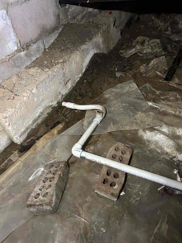 Conducted site assessment of HVAC air handler installation in attic space and crawlspace area to provide estimate for rerouting condensate drainage line. Evaluated existing white PVC condensate piping configuration running through crawlspace with multiple elbows and joints, noting moisture exposure concerns and deteriorated foundation conditions. Documented current air handler setup with connected refrigerant lines, electrical connections, and condensate drain routing to develop comprehensive proposal for relocating drainage system out of compromised crawlspace environment.