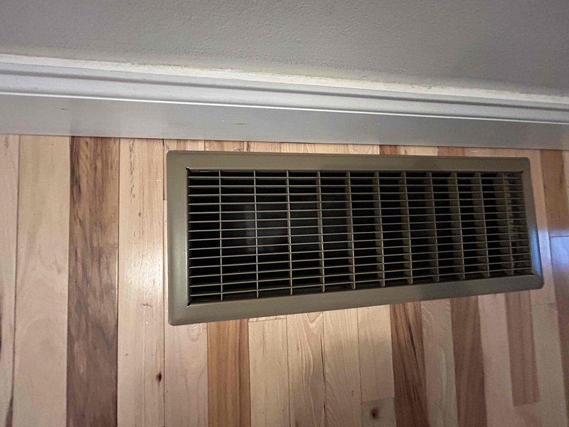 Returned to property for follow-up inspection of HVAC installation with focus on hardwood flooring condition near register locations. Documented wall-mounted vent installation in wood-paneled area and floor register placement in hardwood entryway. Photographed both installations to verify proper integration with finished surfaces and confirm no damage occurred to wood flooring or paneling during system installation.