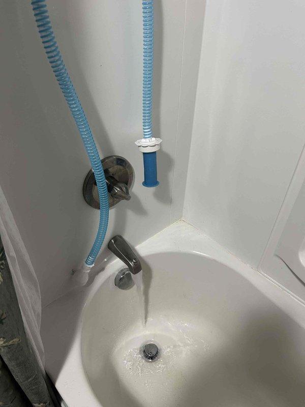 # Plumbing Inspection Summary

Completed routine plumbing inspection at residential property. Documented significant mineral deposit and calcium buildup accumulation on shower tile walls originating from showerhead area, indicating hard water conditions and potential need for water softener evaluation or descaling treatment. Inspected bathtub plumbing connections including wall-mounted fixtures, flexible drainage hoses, and chrome faucet assembly for proper operation and potential leaks.

# Detailed Findings

**Shower Area Inspection:**
Identified extensive mineral deposits, soap scum, and calcium buildup forming cascading patterns down light gray tile walls from showerhead location. Buildup exhibited whitish, crusty texture with areas of discoloration, indicating prolonged accumulation from hard water conditions. Chrome showerhead and wall-mounted wire caddy inspected for proper mounting and functionality. Tile grout lines and corner seams examined for integrity.

**Bathtub Plumbing A