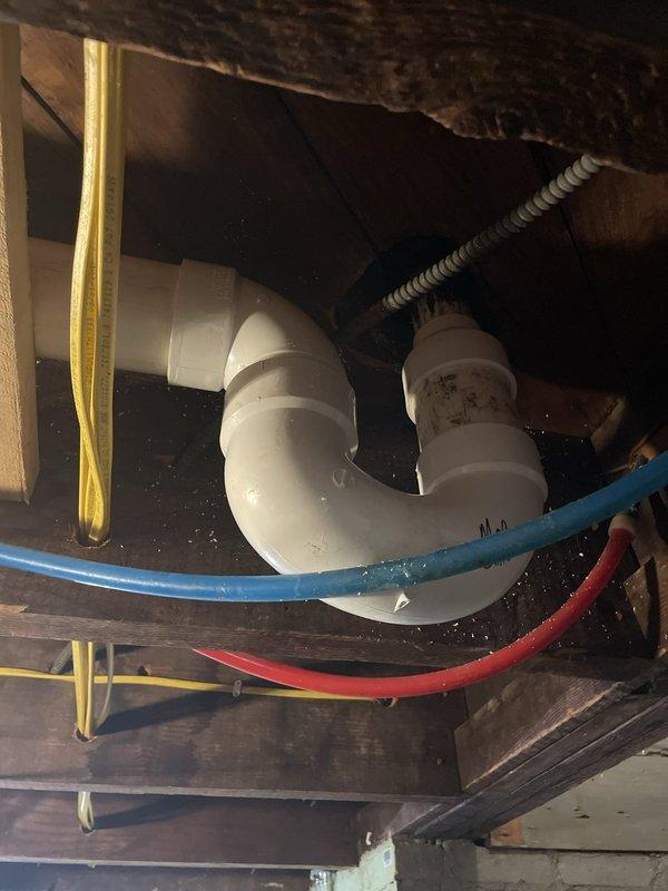 Responded to commercial water leak at mop sink location. Upon inspection, identified active leak in P-trap assembly beneath industrial stainless steel utility sink. Removed existing mop sink unit to access plumbing connections and diagnose source of water intrusion. Inspected white PVC drain configuration and associated trap assembly in crawlspace area. Repaired defective drain connections, replaced worn P-trap components, and verified proper seal on all plumbing fittings. Reinstalled utility sink with chrome wall-mounted faucet and utility hose connections. Tested system for leaks and confirmed proper drainage function. All plumbing connections secured and operational.