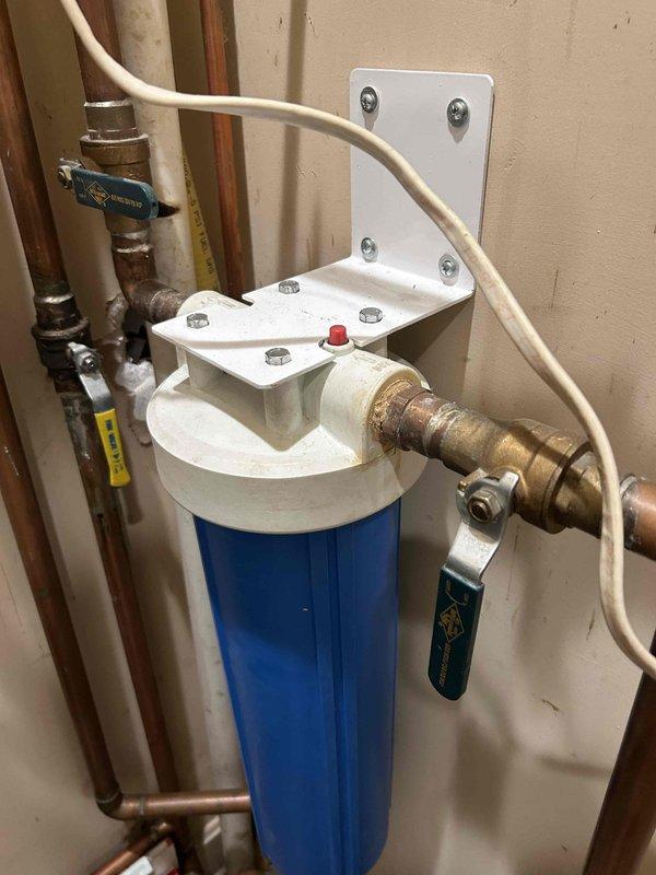 Responded to emergency same-day service call for water leak originating from water heater located in main floor closet. Upon arrival, identified active dripping condition at water heater connections. Inspection revealed significant moisture damage to surrounding wall structure and corner framing, with visible deterioration, dark discoloration, and blue-green staining indicative of prolonged water exposure and potential microbial growth.

Evaluated water filtration system and associated copper piping upstream of water heater. Identified leak source at connection points near filter housing assembly. Shut off water supply using existing ball valves to isolate affected section. Assessed condition of copper piping, brass fittings, and PEX connections throughout the system, noting age-related patina and corrosion at multiple junction points.

Tightened compromised connections and replaced deteriorated fittings as necessary. Verified integrity of water filter housing, mounting bracket, and pr