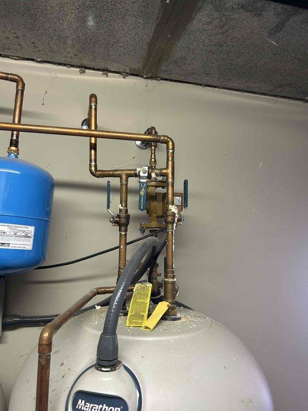 Responded to a no-heat call on a 20-year-old geothermal heat pump system reporting a loud operational noise. Inspected the mechanical room, including the copper water-side piping, isolation valves, and expansion tank, and noted mineral buildup and corrosion at a brass fitting along with flux residue at soldered joints, which may indicate minor leakage or aging components. Further diagnostic testing and component evaluation are recommended to isolate the noise source and restore heating operation.