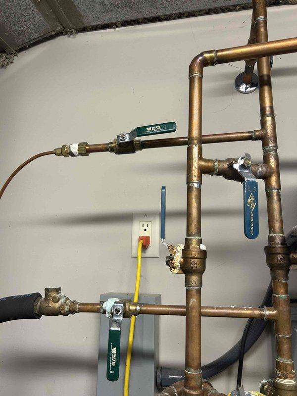 Responded to a no-heat call on a 20-year-old geothermal heat pump system reporting a loud operational noise. Inspected the mechanical room, including the copper water-side piping, isolation valves, and expansion tank, and noted mineral buildup and corrosion at a brass fitting along with flux residue at soldered joints, which may indicate minor leakage or aging components. Further diagnostic testing and component evaluation are recommended to isolate the noise source and restore heating operation.
