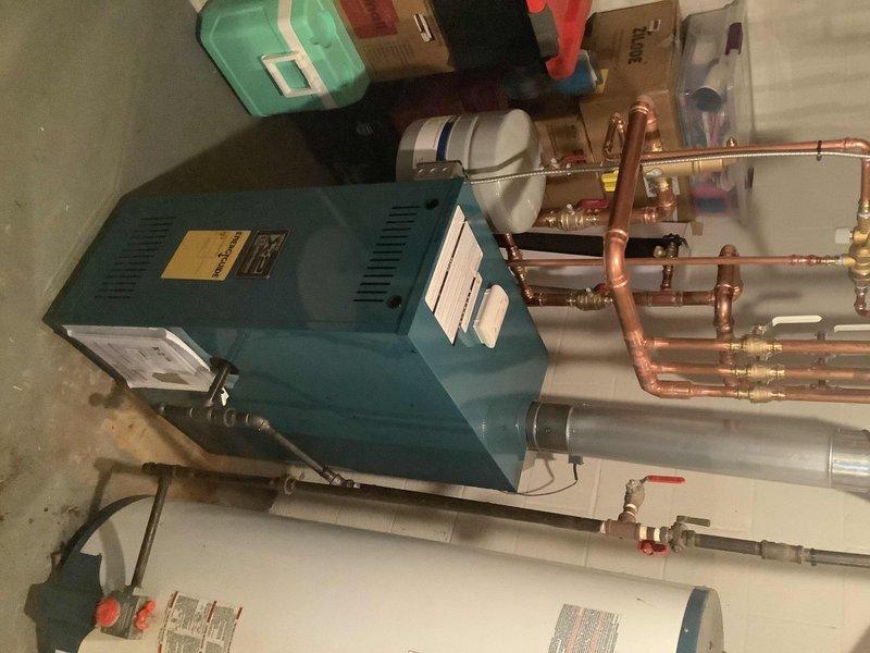 Completed boiler installation with comprehensive piping system setup in basement utility area. Installed new teal/blue boiler unit with associated copper piping network, valves, and fittings, ensuring proper integration with existing water heater. All components properly mounted, connected, and verified operational per installation specifications.