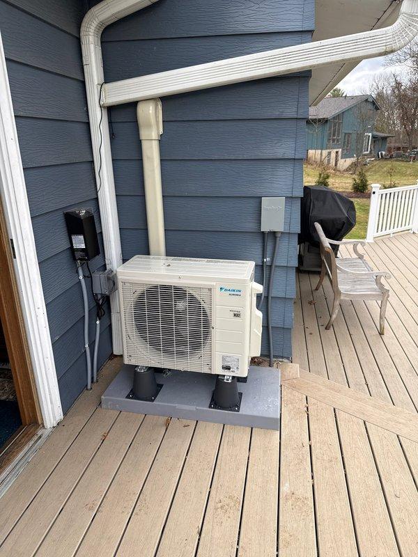 Successfully installed a Daikin single-head mini-split system with the outdoor condenser properly mounted on a concrete pad on the customer's wooden deck. Removed existing wall heater and covered flue with sheet metal as requested, with customer agreeing to complete additional repairs. Professional line-set installation includes proper wall penetration with weather-sealed cover plate and secured PVC line covers.