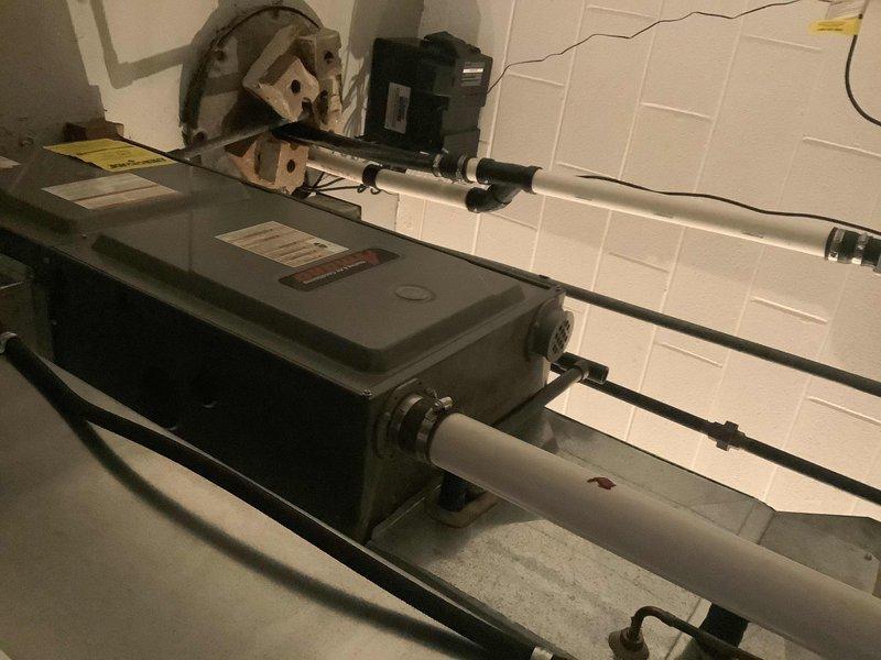 Conducted evaluation of 22-year-old furnace system for potential replacement. Documented existing installation showing aging air handler with PVC ventilation pipes and standard metal ductwork connections. System displays expected wear consistent with age, including visible dust accumulation and minor surface discoloration. Photographed current setup to assist with proper sizing and configuration requirements for replacement proposal.