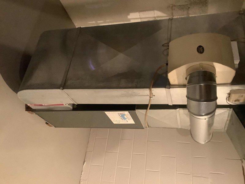 Conducted evaluation of 22-year-old furnace system for potential replacement. Documented existing installation showing aging air handler with PVC ventilation pipes and standard metal ductwork connections. System displays expected wear consistent with age, including visible dust accumulation and minor surface discoloration. Photographed current setup to assist with proper sizing and configuration requirements for replacement proposal.
