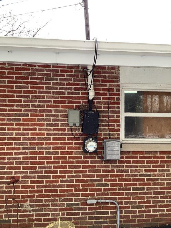 Completed a comprehensive service upgrade involving installation of dual service panels and a 100-amp transfer switch. Removed outdated fuse panel system embedded in wooden wall paneling and replaced with modern circuit breaker panels. Upgraded exterior electrical connections at the meter and junction box on brick exterior wall, ensuring proper connection to utility power lines.