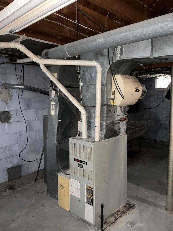 Performed comprehensive assessment of 25-year-old Bryant 89 furnace and AC system in basement utility area. Evaluated existing ductwork configuration, noting potential sizing inadequacies due to home addition. System shows normal wear consistent with age. Documented current installation including furnace unit, connected ductwork network, and PVC venting to determine appropriate replacement options and possible ductwork modifications.