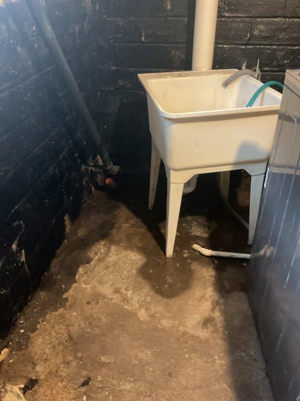 Responded to service call for main drain clog in recently purchased home. Diagnosed standing water issues around utility sink in basement. Cleared obstruction in floor drain near support post, which showed signs of previous water backup and wall discoloration.