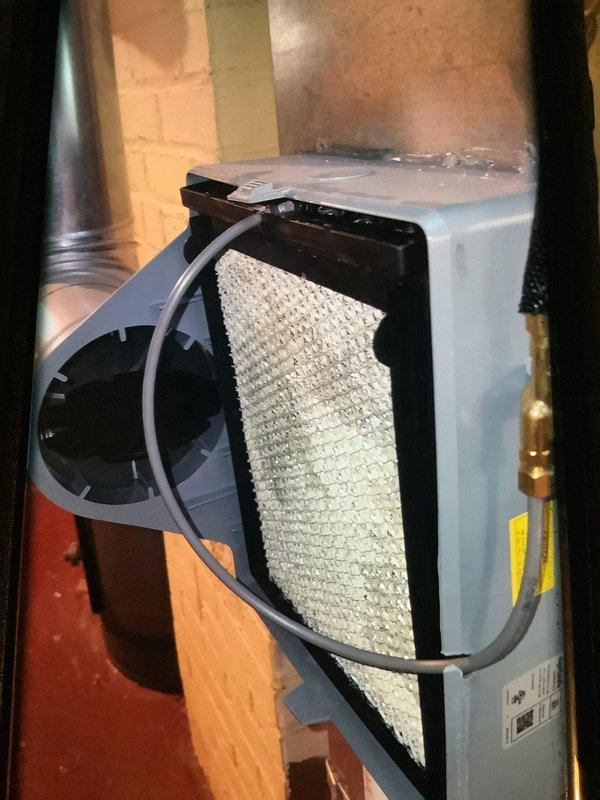 Responded to service call for leaking humidifier. Inspected unit mounted on brick wall and found water leaking from the brass valve assembly. Serviced the connection points where black insulated hoses connect to the valve, resolving the leak issue. Verified proper operation after repair.