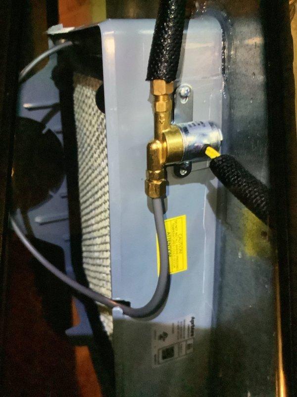 Responded to service call for leaking humidifier. Inspected unit mounted on brick wall and found water leaking from the brass valve assembly. Serviced the connection points where black insulated hoses connect to the valve, resolving the leak issue. Verified proper operation after repair.