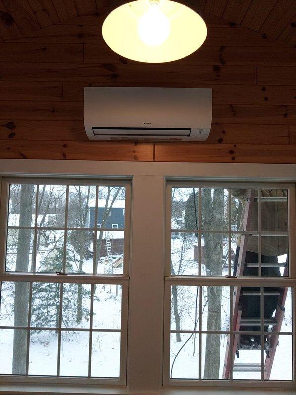 Completed installation of a Daikin mini-split system with two indoor air handlers - one mounted in the wood-paneled main room above windows and another in the secondary room with drop ceiling. Customer retained existing downflow 90% furnace as supplementary heating source.