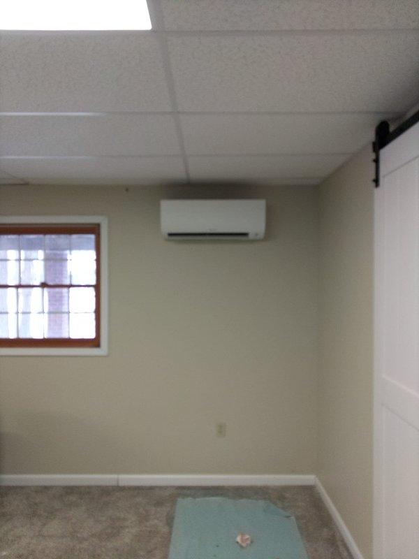Completed installation of a Daikin mini-split system with two indoor air handlers - one mounted in the wood-paneled main room above windows and another in the secondary room with drop ceiling. Customer retained existing downflow 90% furnace as supplementary heating source.