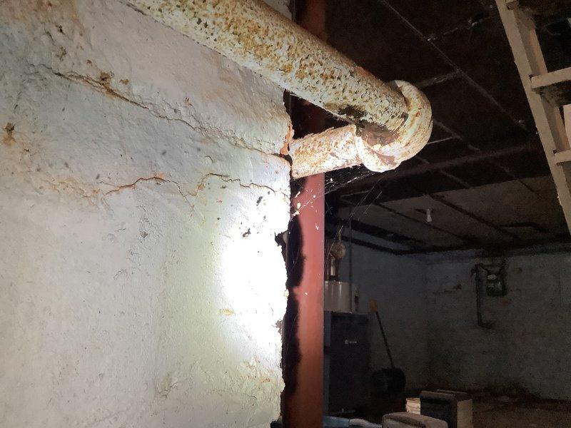 Responded to service call for a leaking radiator in a century-old home. Upon inspection, identified significant corrosion on aging pipes with visible rust deterioration at joint connections. Repaired the leaking section which had caused substantial water damage to the concrete block wall as evidenced by brownish staining and potential mold growth. Recommended comprehensive system assessment due to the advanced age and condition of the plumbing infrastructure.