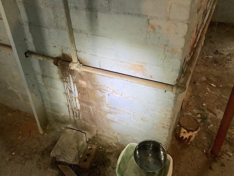Responded to service call for a leaking radiator in a century-old home. Upon inspection, identified significant corrosion on aging pipes with visible rust deterioration at joint connections. Repaired the leaking section which had caused substantial water damage to the concrete block wall as evidenced by brownish staining and potential mold growth. Recommended comprehensive system assessment due to the advanced age and condition of the plumbing infrastructure.