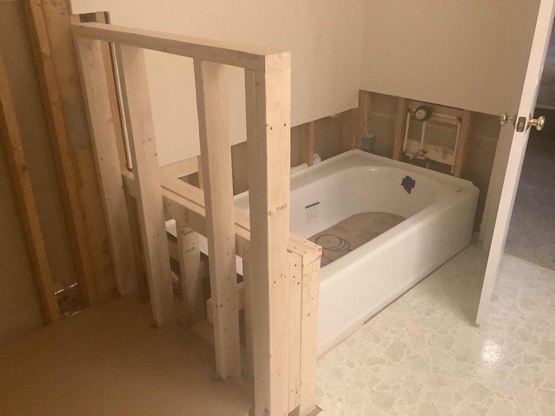 Completed installation of bathroom renovation including framing knee wall between tub and shower, installing 5' x 32" skirt tub, and 4' x 3' shower base. Connected all drain and water lines for both fixtures and prepared mounting areas for customer-supplied Moen Eva deck mount faucet, valve, and shower trim in chrome finish. Customer will complete finish tile work and final knee wall surfacing.