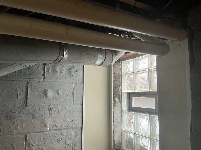 Conducted estimate for replacement of 17-18 year old furnace system in basement utility area. Inspected existing dual-unit HVAC configuration with PVC venting and documented corrosion issues on metal piping. Evaluated ductwork and ventilation system throughout the space, noting glass block window location for potential ventilation considerations.