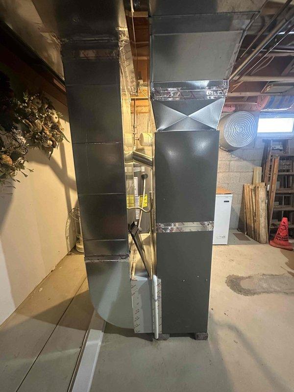 Completed installation of a new 80% furnace and air conditioning system in residential basement. System includes properly sealed galvanized sheet metal ductwork with metallic tape at joints connecting to the air handler. Carbon monoxide detector was installed and tested to ensure occupant safety.