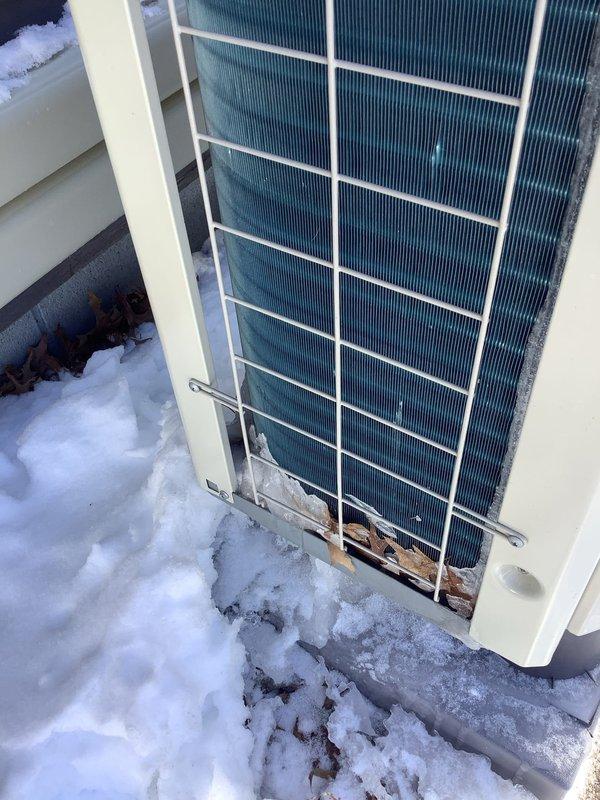 Diagnosed mini split outdoor unit failure on a 4-month-old installation. Observed significant snow and ice accumulation against the condenser coil, with debris trapped between the protective grill and coils. Noted signs of moisture buildup and possible rust formation at the base of the unit where snow had partially melted and refrozen against the equipment.