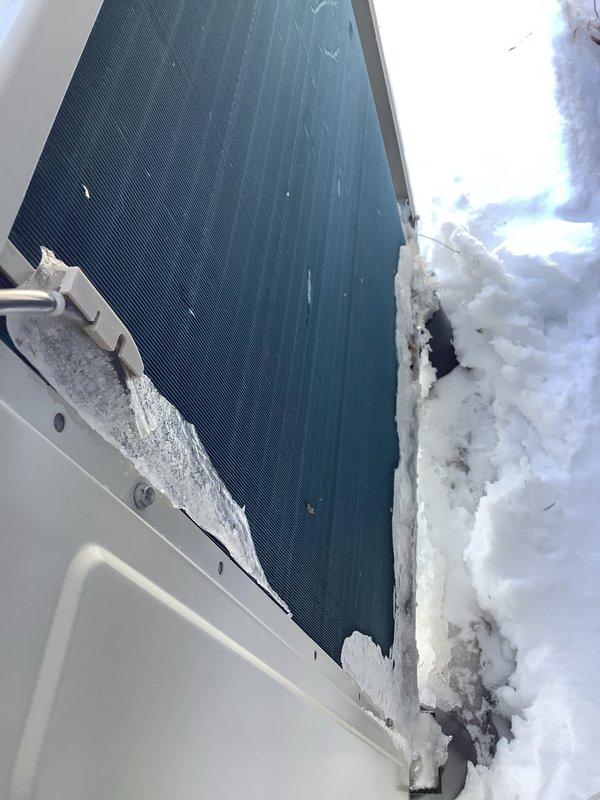 Diagnosed mini split outdoor unit failure on a 4-month-old installation. Observed significant snow and ice accumulation against the condenser coil, with debris trapped between the protective grill and coils. Noted signs of moisture buildup and possible rust formation at the base of the unit where snow had partially melted and refrozen against the equipment.