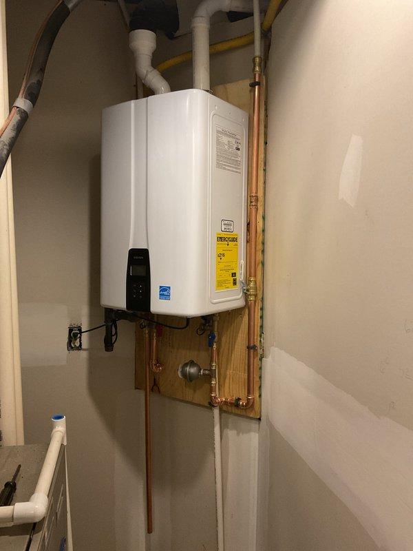 Successfully installed a Navien NPE-240A2N(G) tankless water heater with all necessary components. Complete installation included proper mounting on wooden backing board, connection of copper supply lines with brass fittings, and installation of PVC venting system. Unit is operational with Energy Star certification.