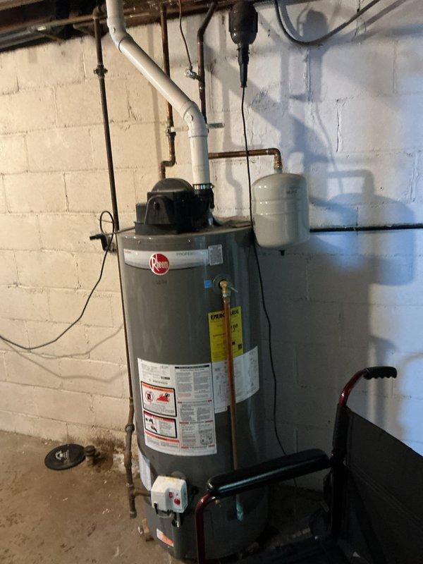 Performed diagnostic inspection on leaking Rheem tanked water heater. Confirmed water leakage from bottom of unit, indicating tank failure. Documented condition with photos showing installation configuration including PVC and copper piping connections, expansion tank, and basement drainage system. Recommended complete replacement of failed water heater.