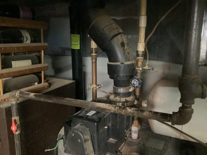 Performed diagnostic assessment on residential water heater system showing signs of wear at connection points. Inspected copper piping connections to tank and examined PVC plumbing components. Identified and repaired leaking joint at black PVC elbow pipe near the Arcoaire furnace unit, restoring proper function to the water heating system.