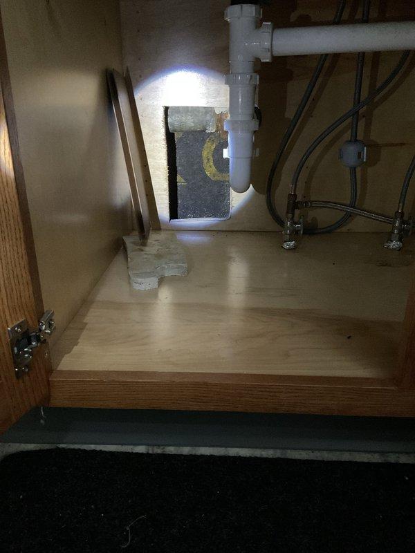 Responded to service call for kitchen sink leak affecting lower level. Inspection revealed water damage to ceiling/wall with exposed wooden framing. Examined under-sink plumbing system including PVC drain assembly and supply lines. Repaired leaking connection to prevent further water infiltration and structural damage.