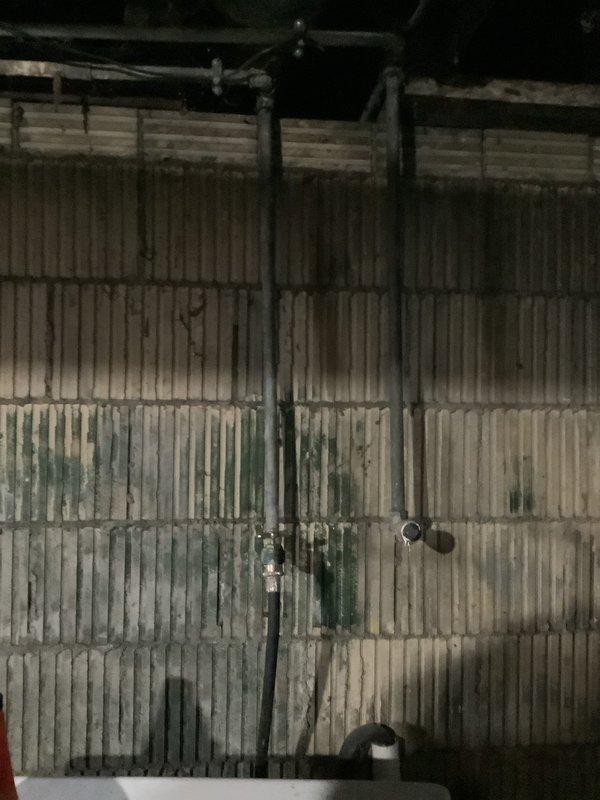 Conducted inspection of plumbing system in utility area with focus on toilet replacement needs. Assessed current installation and confirmed quote details for new American Standard Champion toilet (1.6 GPF, elongated bowl, comfort height). Documented existing conditions including water damage on corrugated metal wall panels and examined exposed ceiling infrastructure with PVC piping. Customer requires additional estimates for other plumbing work.