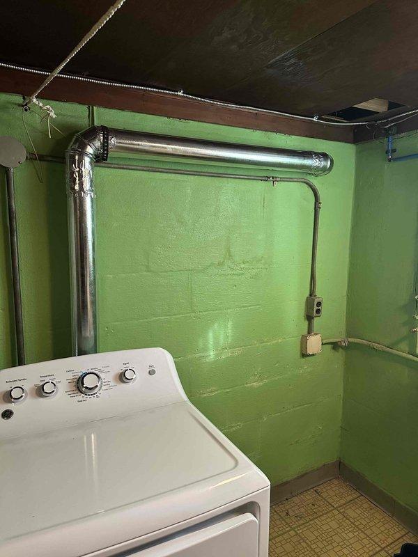 Completed installation of rigid metal dryer vent ductwork in basement laundry area, replacing non-compliant flexible hose to meet city code requirements for electric dryer ventilation. System includes properly sealed 90-degree elbow joints and secure wall mounting for optimal airflow in this 60+ year old residence.