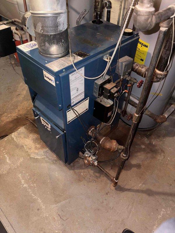 Performed inspection of 1998 steam boiler system exhibiting flame rollout issues at front of unit. Observed significant plugging in heat exchanger. Documented condition with photos of boiler assembly and surrounding mechanical area. System requires replacement due to safety concerns; boiler efficiency rating at 89%.