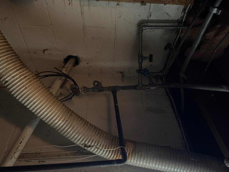 Completed main water valve replacement in customer's basement utility area. Accessed valve near cinder block wall where water line enters property, working around existing ductwork and pipe infrastructure. Service restored water functionality to the home after city water was shut off for the repair.