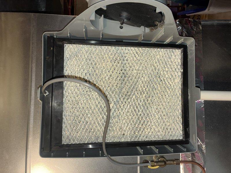 Performed scheduled MVP heating maintenance service. Inspected utility space plumbing infrastructure and heating system components. Examined humidifier assembly, noting filter pad showing normal wear with slight discoloration; all connections and fittings remain secure and functional.