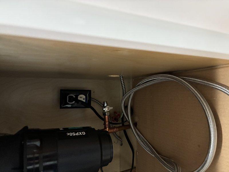 Installed electrical wiring for under-cabinet fixture, running flexible metal conduit from junction box to the designated location. Connected power supply to GXP50C unit, ensuring proper electrical connections while coordinating with existing plumbing components in the enclosed cabinet space.