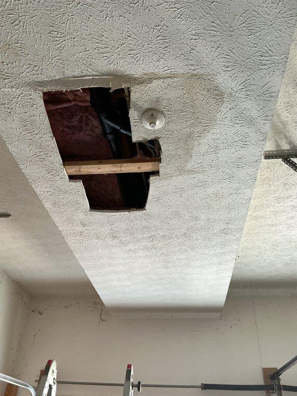 Repaired a frozen and split CPVC tee in garage ceiling by cutting out the damaged section and rebuilding the connection from the 3/4" main line to both 1/2" water lines. Installation included new shut-off valves and required creating access through ceiling drywall to reach the affected plumbing in the joist space.