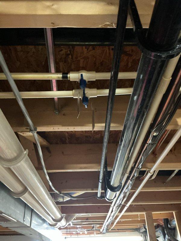 Repaired a frozen and split CPVC tee in garage ceiling by cutting out the damaged section and rebuilding the connection from the 3/4" main line to both 1/2" water lines. Installation included new shut-off valves and required creating access through ceiling drywall to reach the affected plumbing in the joist space.
