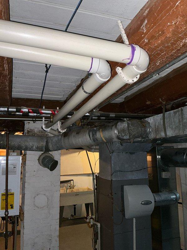 Conducted furnace replacement estimate for 13-year-old Armstrong system in older home with potential construction challenges. Inspection revealed exposed ductwork in utility area with electrical cables running alongside, as well as PVC plumbing infrastructure with purple markings at joints. Noted existing mechanical unit (possibly a humidifier) that would need to be integrated with any new installation.
